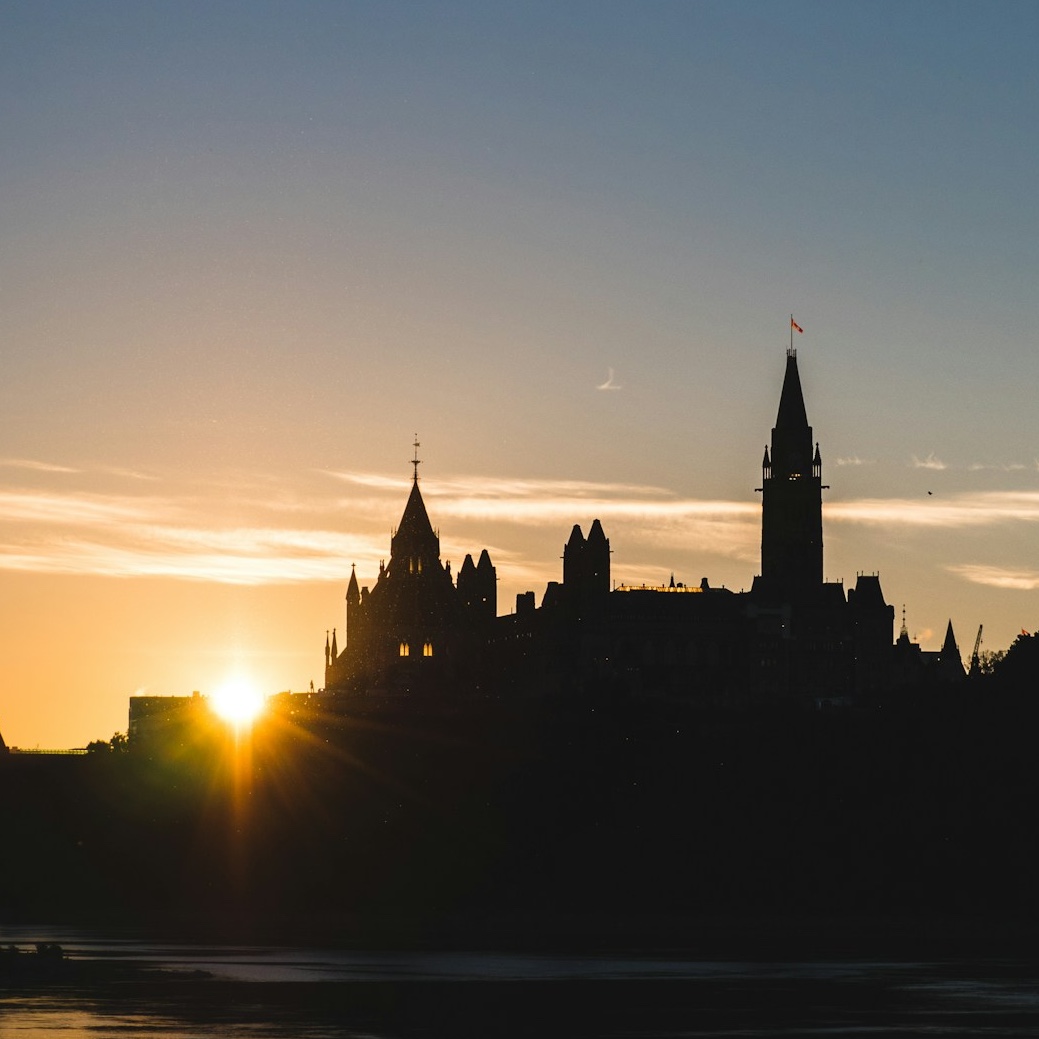 A silhouette of the Canadian House of Commons and Peace Tower near the river during sunrise,